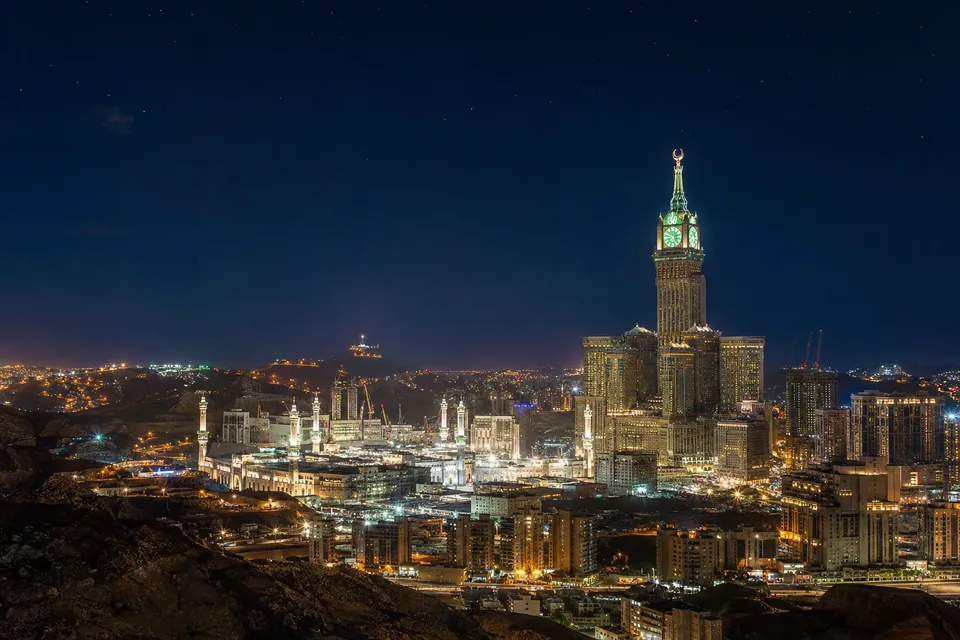 Gece aydınlatılmış saat kulesi ve Mescid-i Haram minareleriyle Mekke silueti